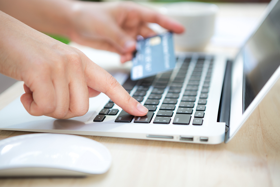 Hands holding a credit card and using laptop computer for online shopping.